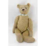 A gold plush teddy bear, with long snout, hump, long arms, stitched features and button eyes,