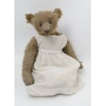 A gold plush teddy bear, with long snout, stitched features and button eyes and long arms,