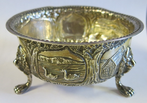 A silver circular bowl, embossed with a fox, birds and buildings, with lion mask and paw feet,