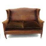A leather upholstered two seat sofa, with wing sides and fabric cushions,