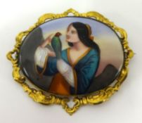 A Continental porcelain brooch decorated with a figure holding an exotic bird in yellow metal ornate