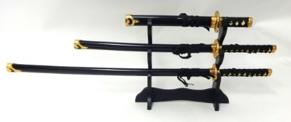 Set of three reproduction Samurai swords on stand