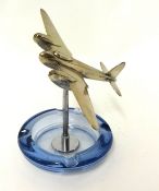 A glass ashtray surmounted with a model of a chromed mosquito aeroplane