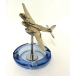 A glass ashtray surmounted with a model of a chromed mosquito aeroplane