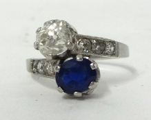 A sapphire and diamond two stone crossover Ring, claw set with a mixed cut stone measuring 7 x 6