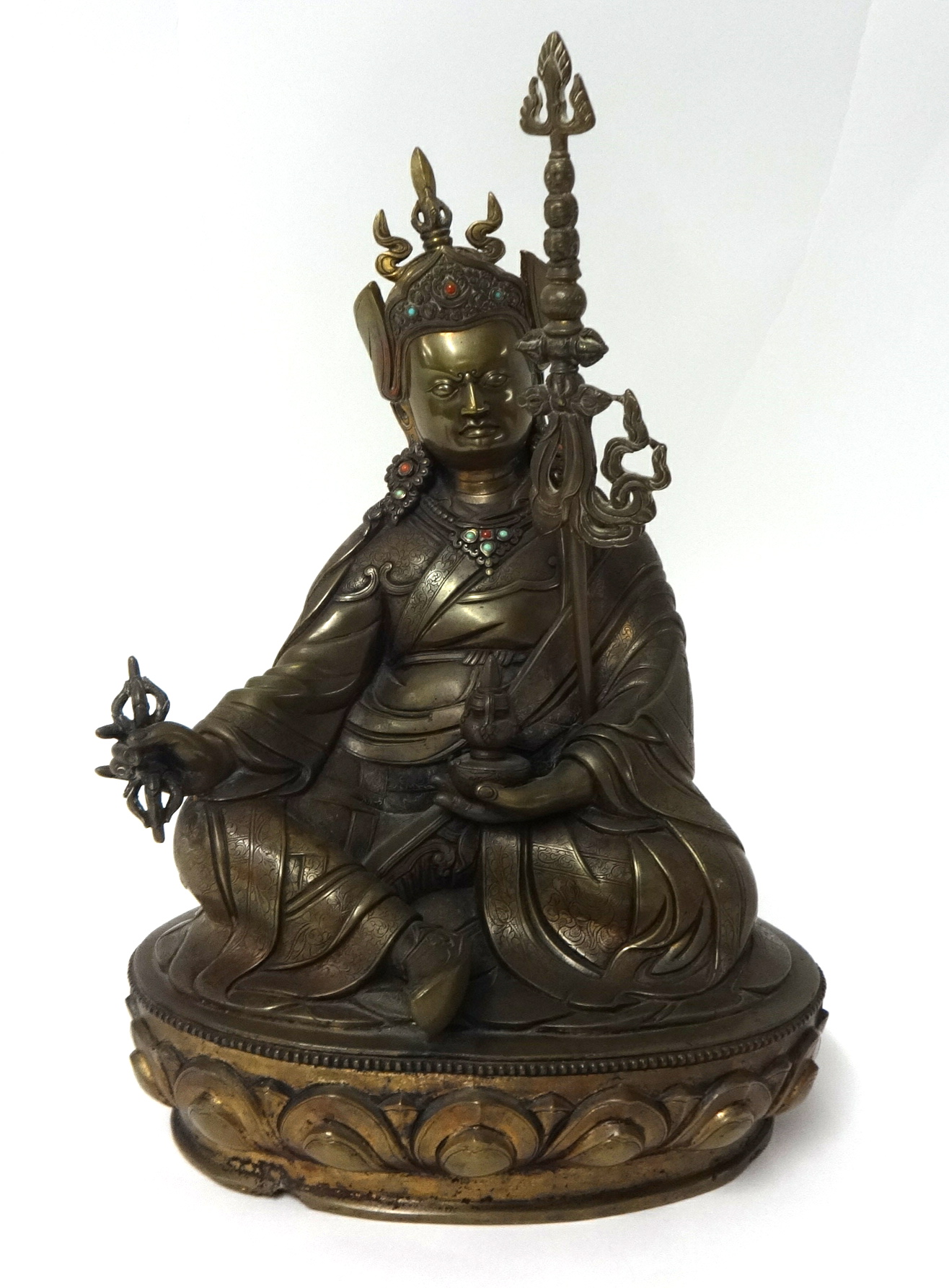 A Tibetan bronze figure of Lama seated on a lotus throne wearing robes and peaked hat, headdress