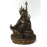 A Tibetan bronze figure of Lama seated on a lotus throne wearing robes and peaked hat, headdress
