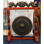 A Chinese floor standing dinner gong with ornate carved and red painted wood stand surmounted with a