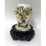 A German porcelain vase of three cherubs encrusted in flowers also a Chinese hardwood urn stand of