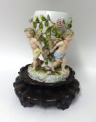 A German porcelain vase of three cherubs encrusted in flowers also a Chinese hardwood urn stand of