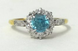 A blue zircon and diamond cluster ring, claw set with a circular cut stone bordered by diamonds,
