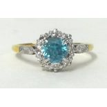 A blue zircon and diamond cluster ring, claw set with a circular cut stone bordered by diamonds,