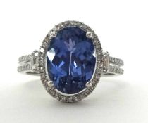 A 14k white gold tanzanite and diamond cluster ring, claw set with an oval mixed cut stone estimated