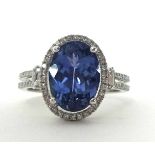 A 14k white gold tanzanite and diamond cluster ring, claw set with an oval mixed cut stone estimated