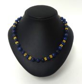 A lapis lazuli bead and gold necklace, composed of 60 uniform beads of 8 mm diameter, with