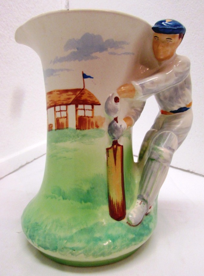 Burleigh Ware pottery cricket jug painted green and cream, the handle moulded as batsman,