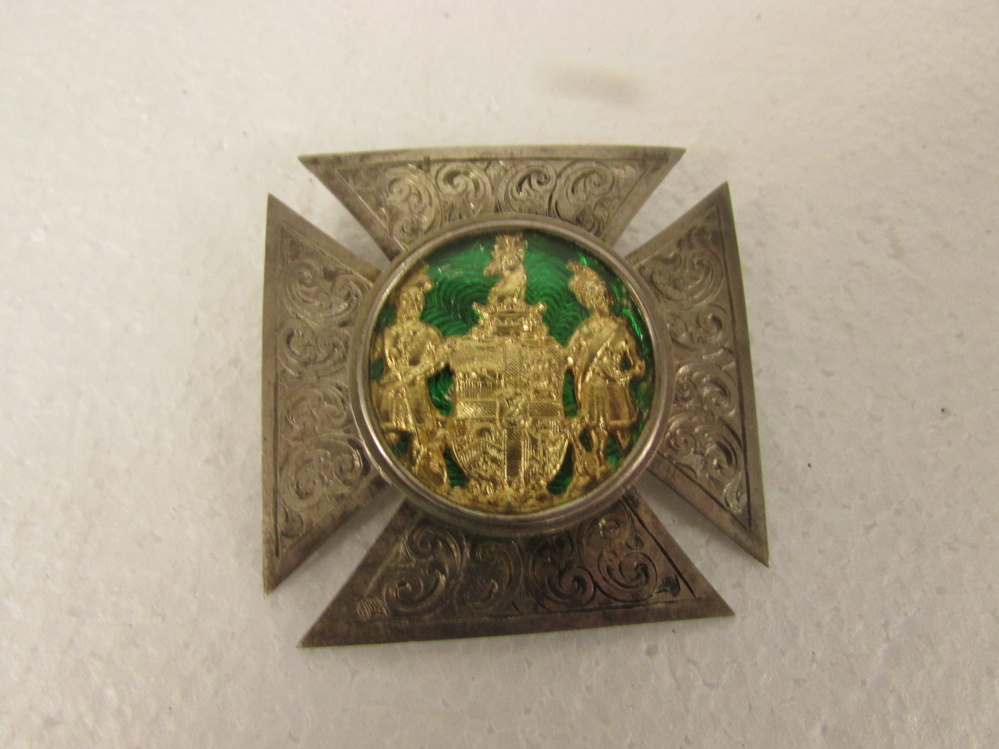 Cruciate white metal Masonic brooch set with a glazed circular emblem of gilded figures flanking