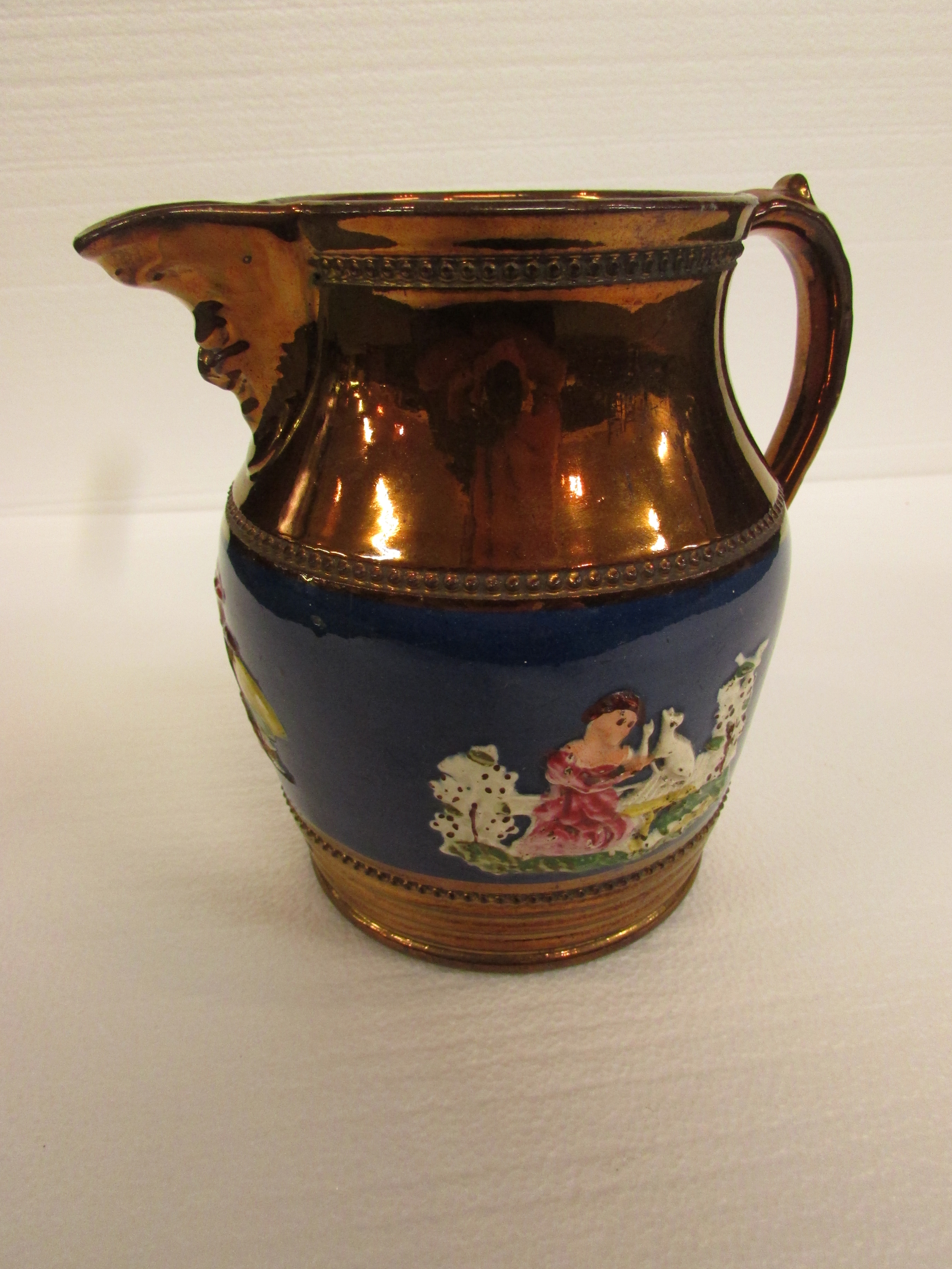 A 19th century copper lustre jug with a band of blue glaze with seated girl and dog in relief