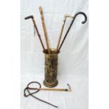 A brass stick stand with embossed bucolic decoration, containing a walking cane with silver