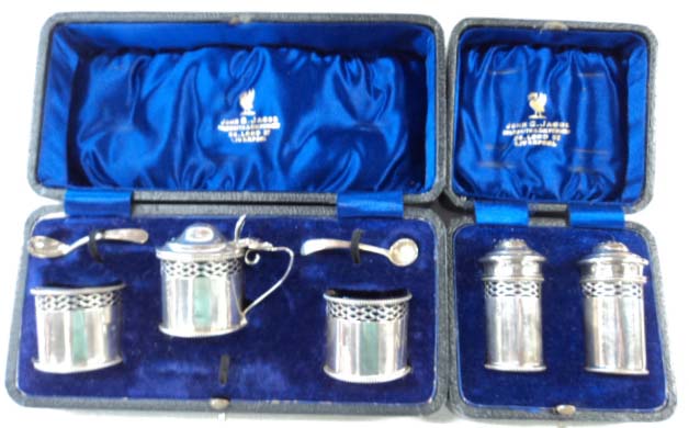 A cased silver three piece condiment comprising a flip top mustard top and pair of salts, with