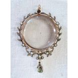 An unmarked gold framed circular pendant, with central glass panels within a seed pearl set wreath