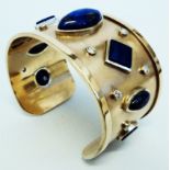 A bespoke yellow metal bangle, set with ten diamonds and seven lapis lazuli panels