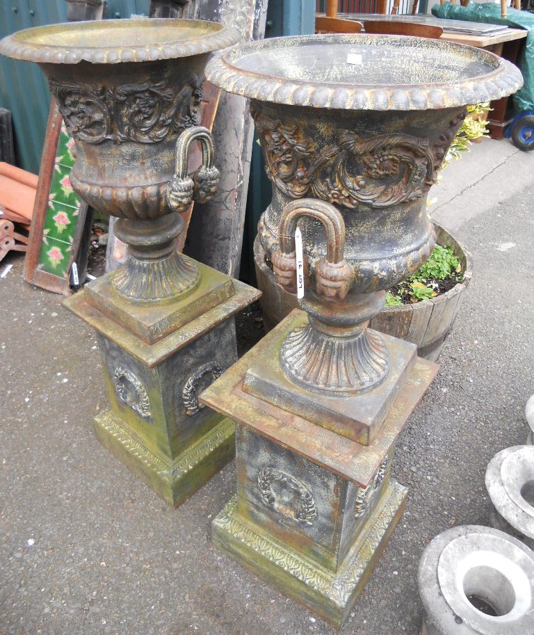 A pair of cast iron garden urns with foliate scroll decoration and flanking handles, set on plinth