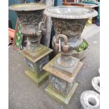 A pair of cast iron garden urns with foliate scroll decoration and flanking handles, set on plinth