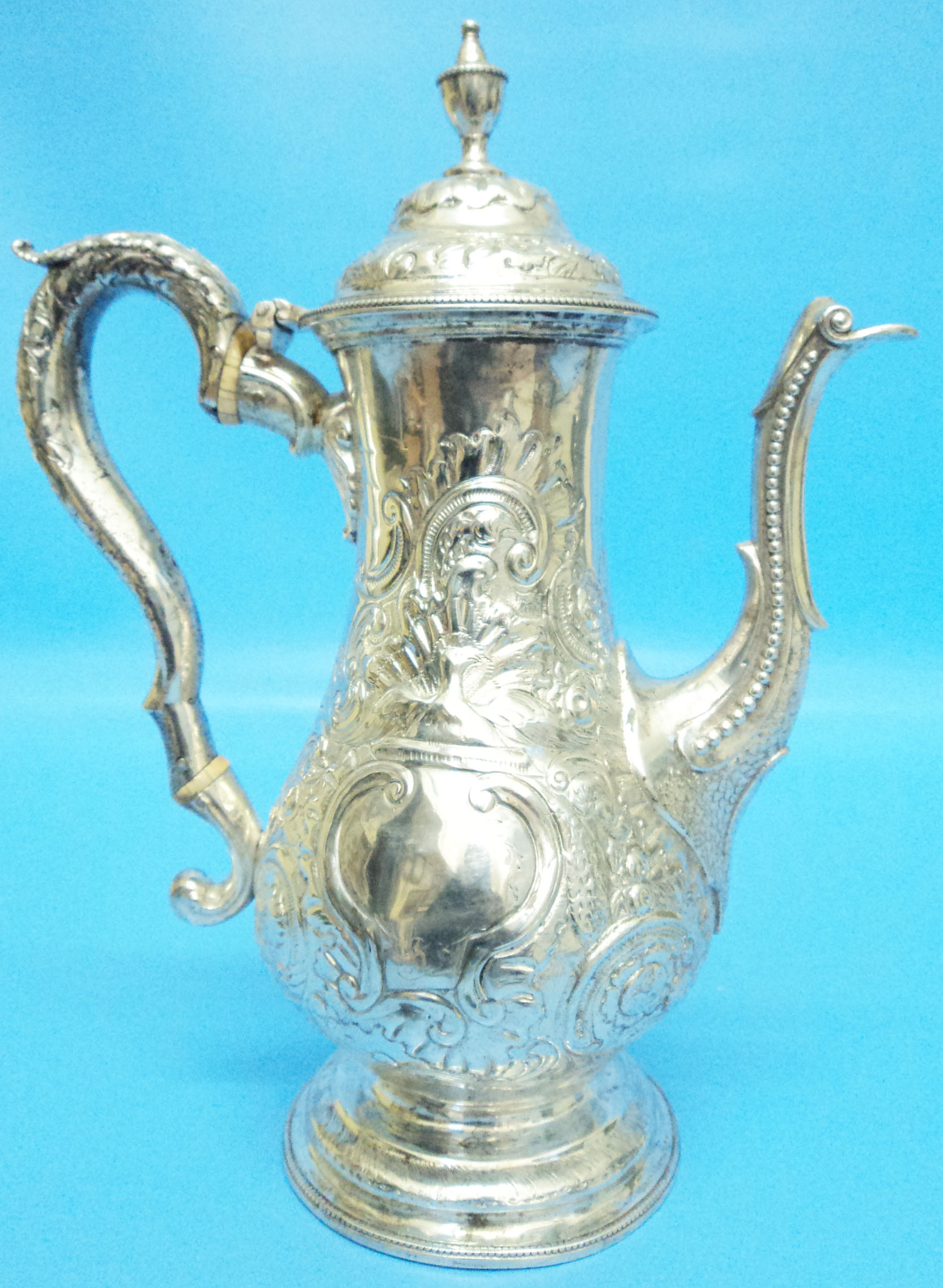 An 18th Century silver coffee pot of slender baluster design, with flip top and embossed C-scroll