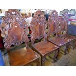 A set of four mahogany and stained wood framed ornate hall chairs, with carved scroll decoration