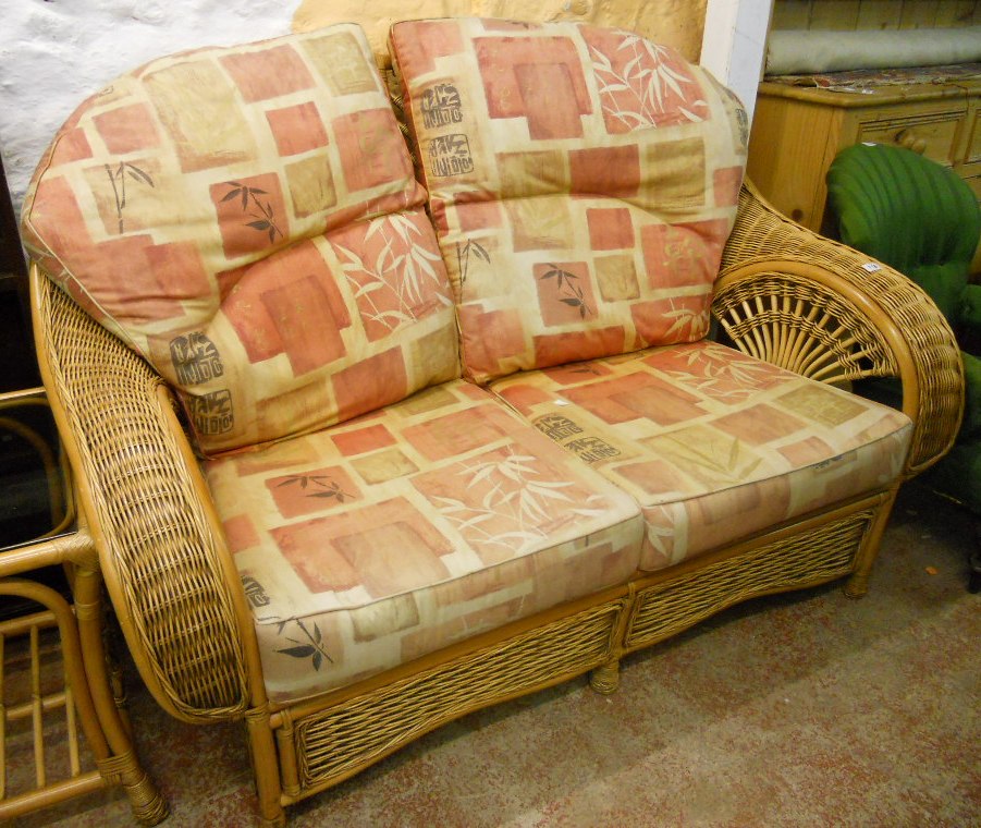 A cane and wicker framed conservatory suite, comprising a two seater settee and pair of armchairs