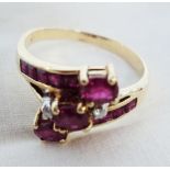 An 18ct. gold cross-over ring, set with three oval rubies, flanking small diamonds and ruby paved