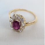 An unmarked high carat gold ring, set with central oval ruby within a ten stone diamond border