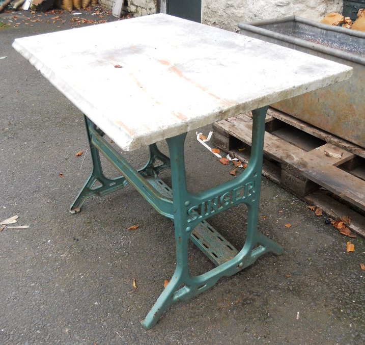 A marble table top set on a painted metal Singer sewing table base