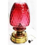 A brass table oil lamp with squat reservoir base, chimney and dimpled cranberry glass shade -