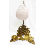 A Rococo style brass desk stand surmounted by a lamp with opaque pink glass shade