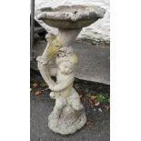 A reconstituted concrete bird bath in the form of a cherub holding a lily