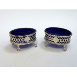 A PAIR OF SILVER TABLE SALTS, London 1896, oval openwork shape with claw feet and blue glass liners,