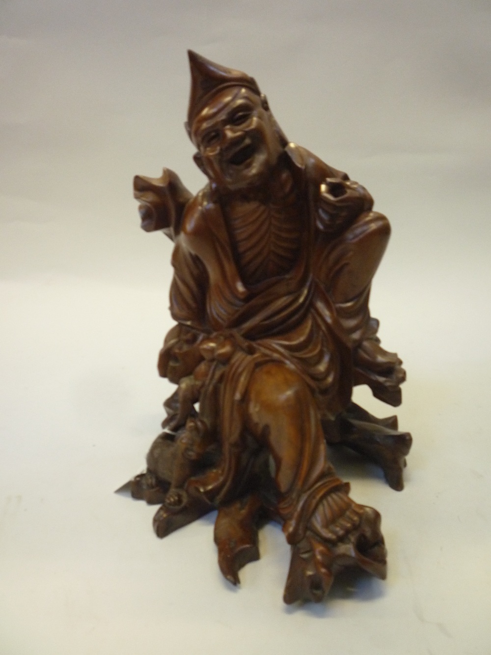 A CHINESE CARVED ROOTWOOD FIGURE OF ZHONGLI QUAN, modelled seated on a knotty tree stump, a small