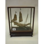 A CHINESE SILVER MODEL OF A WARSHIP, on carved wood base and glazed cabinet, 19th/20th Century