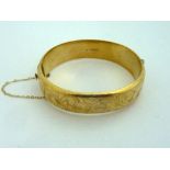 A 9CT GOLD HINGED BANGLE, with scrolling decoration to one side, diameter 62cm, hallmarks for