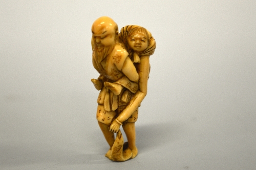 A JAPANESE IVORY NETSUKE, figure of an old man carrying an old lady who is holding a fish