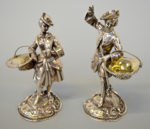 A PAIR OF VICTORIAN SILVER SALTS, each well cast as a gentleman and lady dressed in clothes out on a