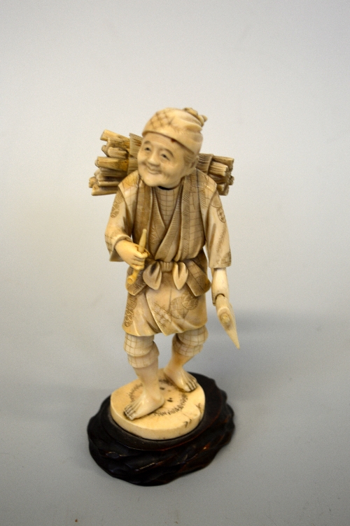 A JAPANESE IVORY OKIMONO MAN CARRYING STICKS, on hardwood base, approximate height 19cm