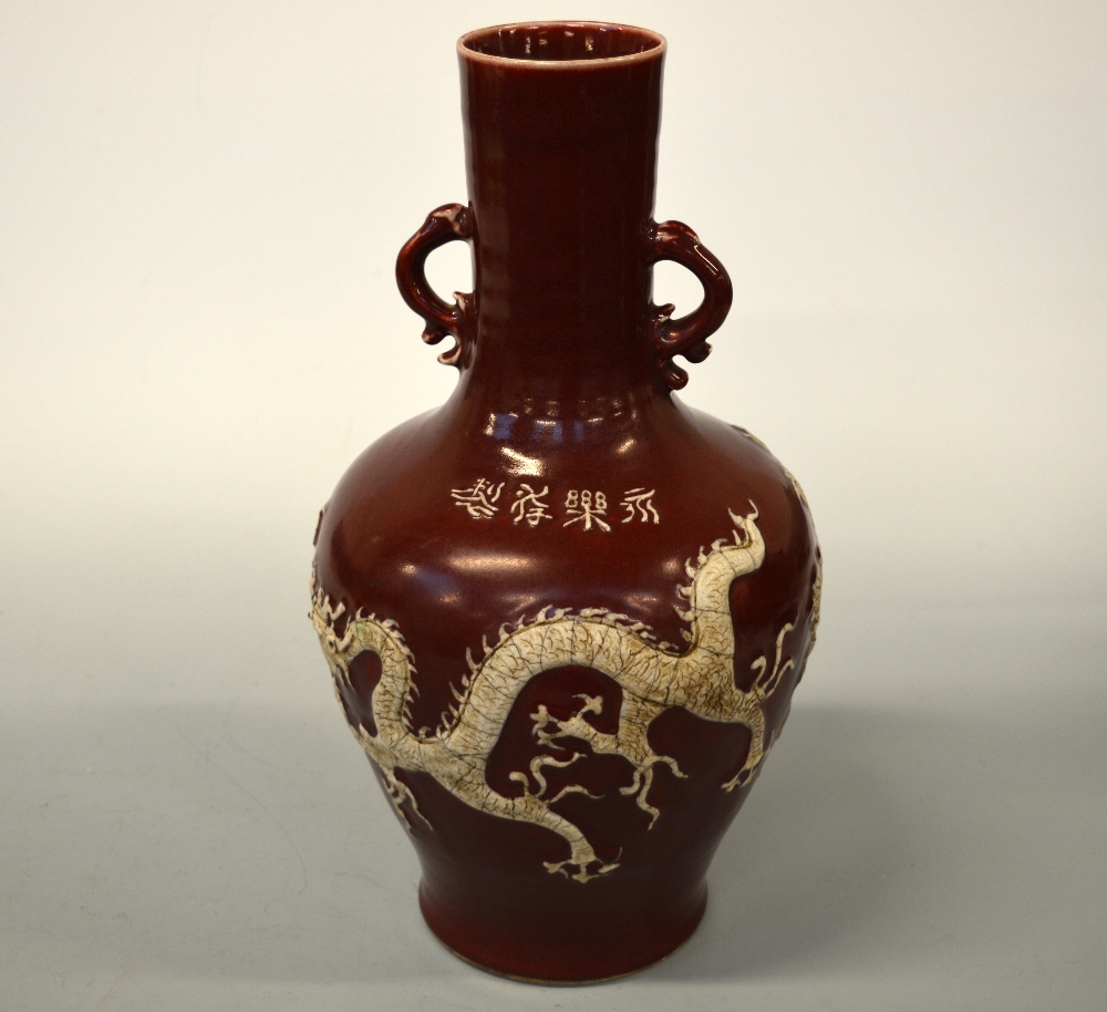 AN ORIENTAL RED GROUND VASE, with dragon and flower decoration in relief, four character script to