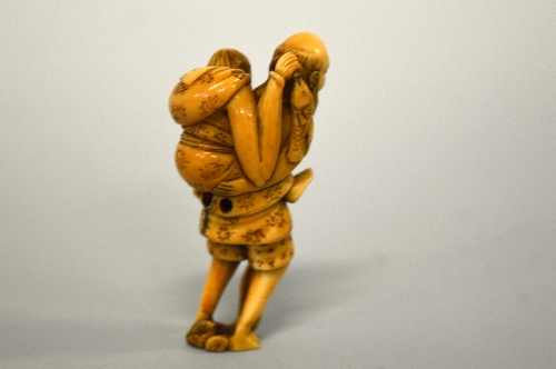 A JAPANESE IVORY NETSUKE, figure of an old man carrying an old lady who is holding a fish - Image 2 of 3