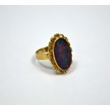 AN OPAL TRIPLET RING, of oval shape within a fancy scalloped border to the plain band, stamped