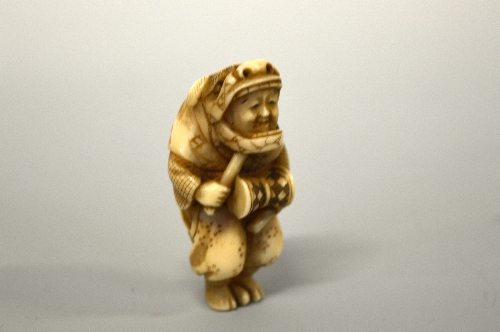 A JAPANESE IVORY NETSUKE, figurine dressed, in a Shi Shi dog mask banging a drum - Image 2 of 3