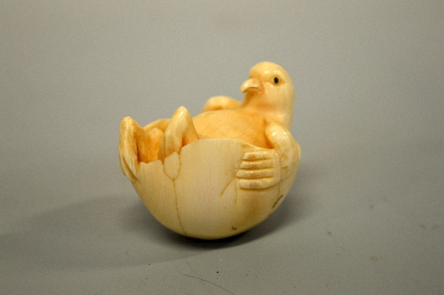 A JAPANESE IVORY NETSUKE, carved in the form of a bird relaxing in an egg, signed to base