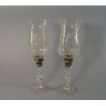 A pair of Stuart Crystal candlesticks with faceted stems, on spreading feet, with storm shades